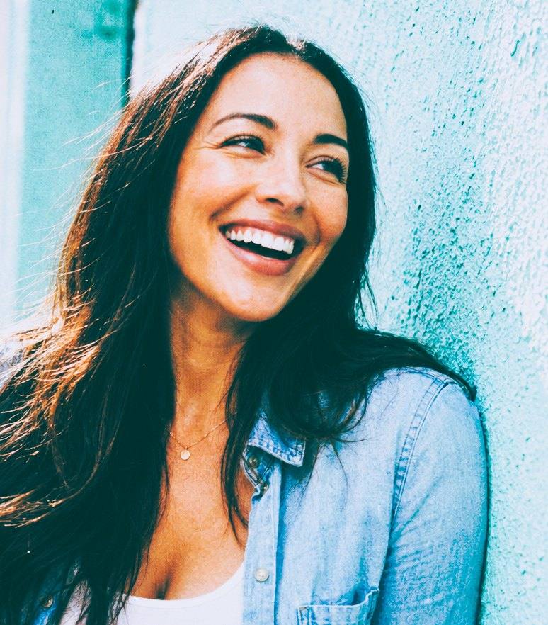 Karla laughing against a sunlit turquoise wall